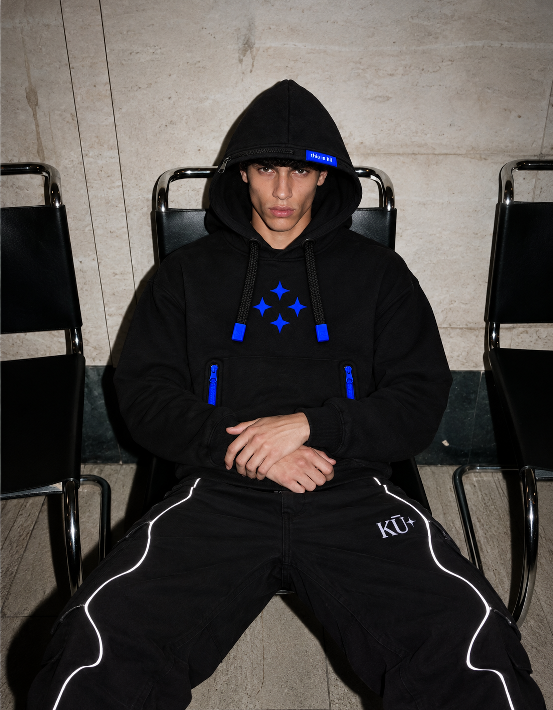Modelo sentado con la sudadera negra Kū Star Hoodie